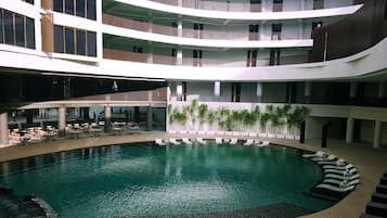 A multi-level indoor swimming pool with lounge areas and a restaurant on the lower level.