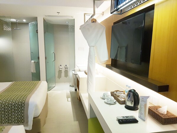 Una habitación de hotel con cama, baño con ducha, televisor, cafetera y control remoto.