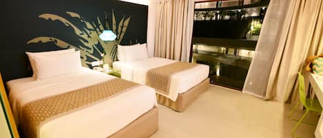 Habitación de hotel con dos camas, un ventanal con cortinas, una planta y una mesita.