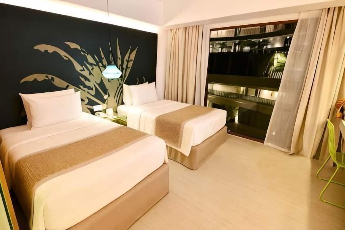 A hotel room with two beds, a nightstand, a plant, and a balcony with curtains.