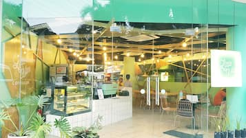 Una cafetería con fachada verde, escaparate de cristal y zona de estar en su interior.