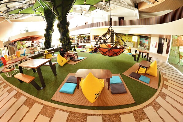 A spacious indoor area with multiple seating arrangements, including tables and chairs, surrounded by a central tree and hanging chairs.