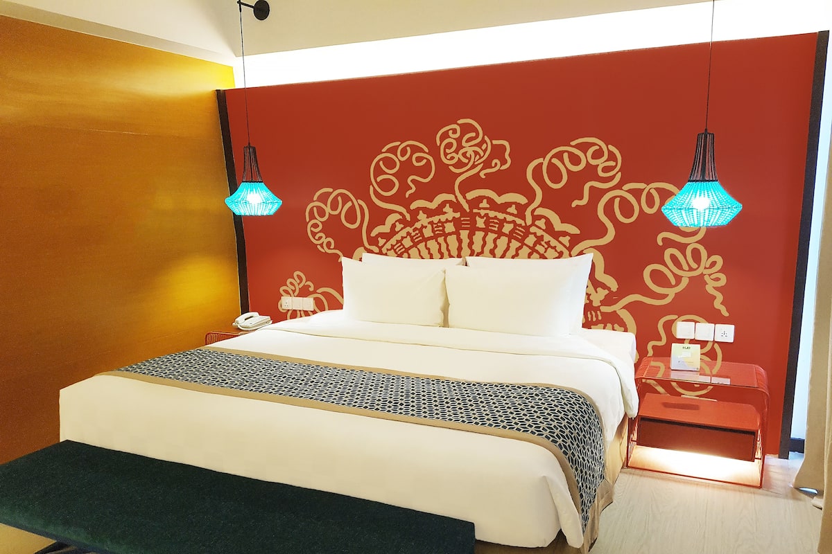 A hotel room with a bed, bedside table, lamp, and a bench.
