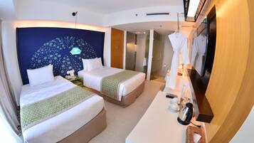 A hotel room with two beds, a desk with a mirror, and a shower area.