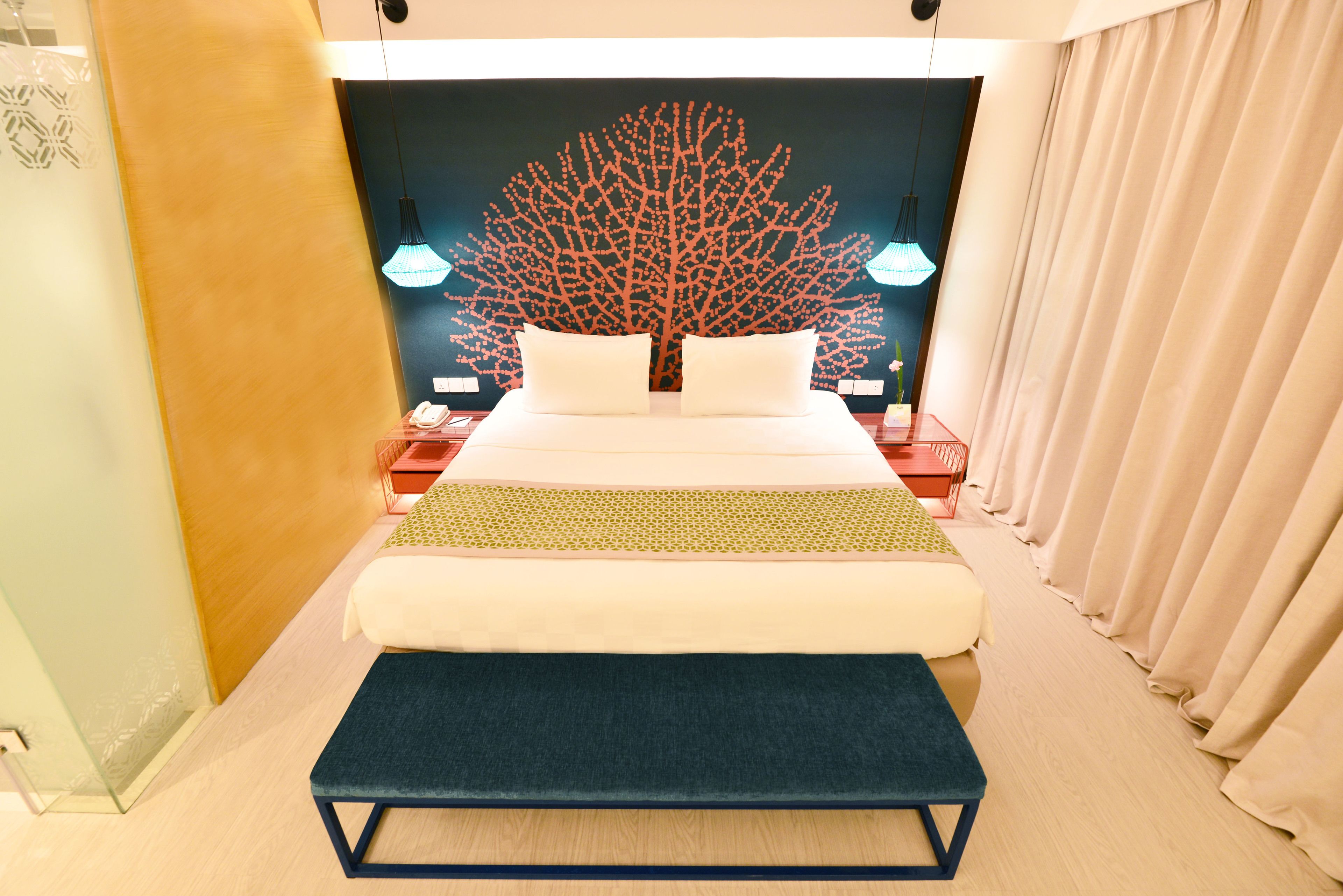 A modern hotel room with a large bed, bedside lamps, a nightstand, and a decorative tree wall.