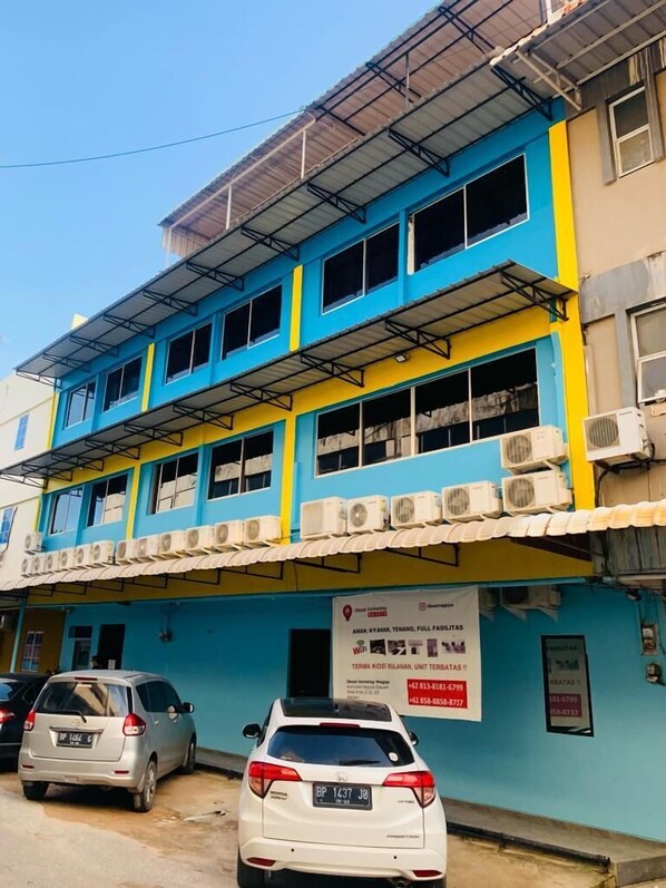A multi-story building with a blue and yellow facade, several air conditioning units, and a sign advertising a home rental service.