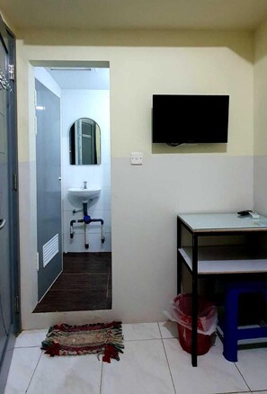 A room with a white sink, a mirror, a television mounted on the wall, and a small table with a stool.