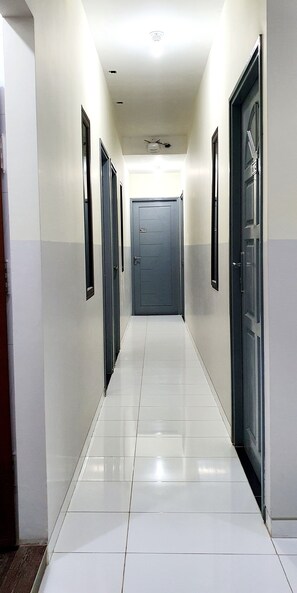A clean, well-lit hallway with white tiled floors and dark-colored doors.
