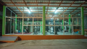 Un gimnasio con equipo de ejercicio, amplias ventanas y fachada verde y naranja.