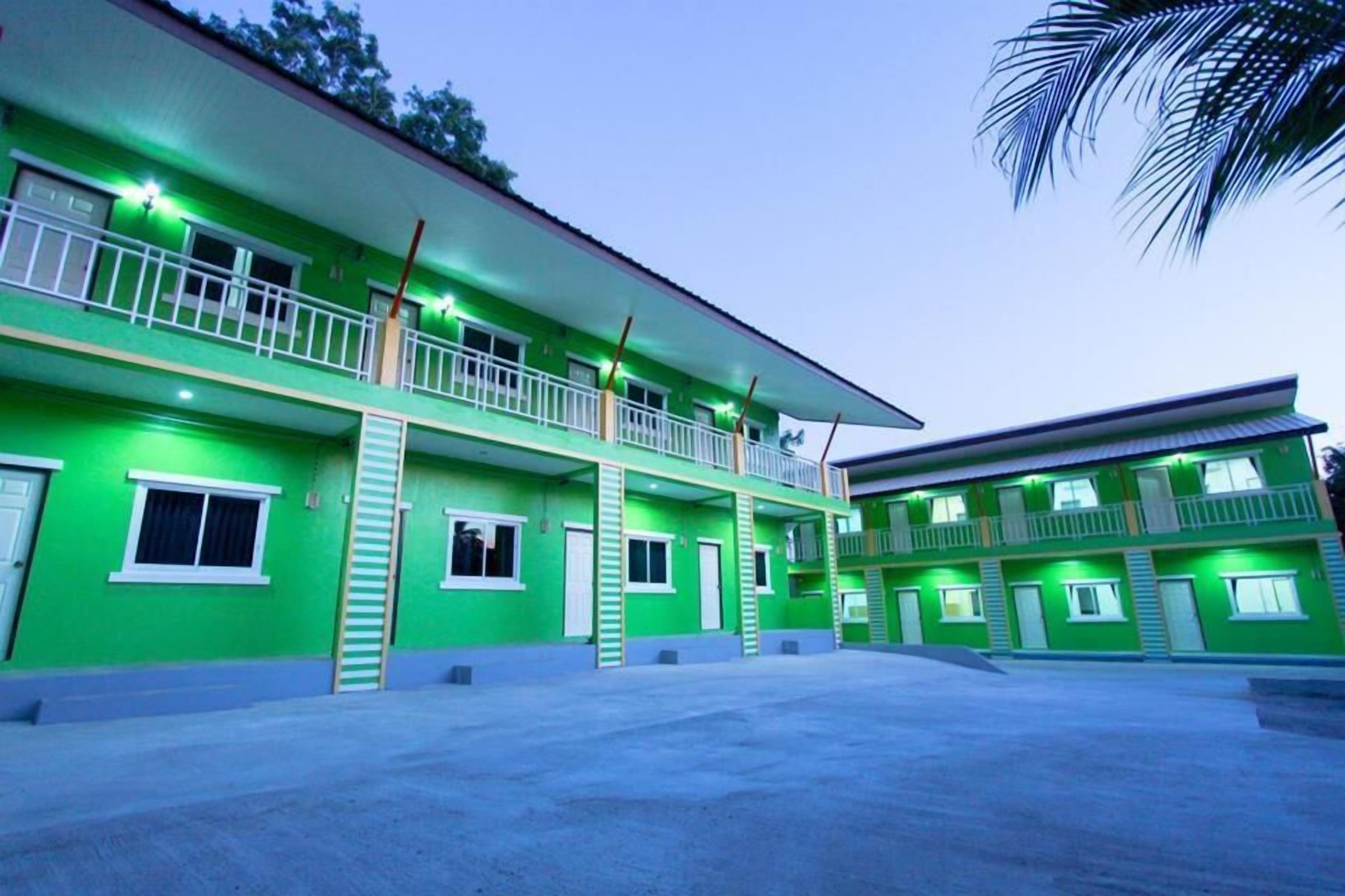A multi-story hotel with a green facade, balconies, and a covered outdoor area.