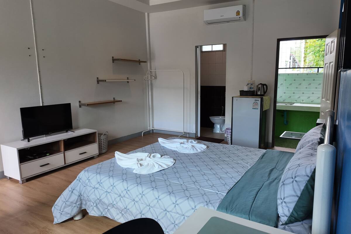A bedroom with a bed, a TV, a wardrobe, a small kitchenette, and a bathroom visible through an open door.