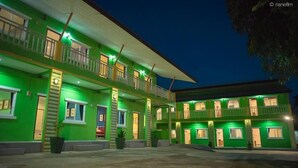 Un edificio de dos pisos con varias habitaciones y balcones, iluminado con luz verde.