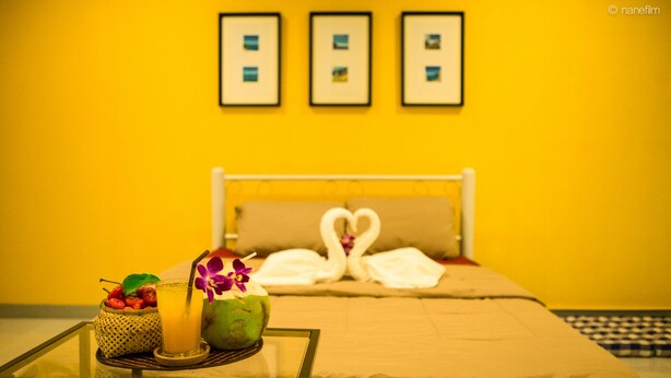 Una cama con sábanas blancas y dos toallas con forma de cisne, un vaso de jugo de naranja, un coco y una cesta de fruta sobre una mesa.