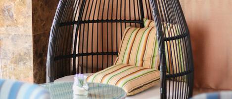 A black wicker chair with a cushion, a glass table, and striped pillows.