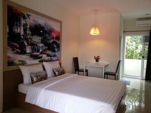 A hotel room with a large bed, a desk, and a chair. There is a painting on the wall and a window with a view of greenery.