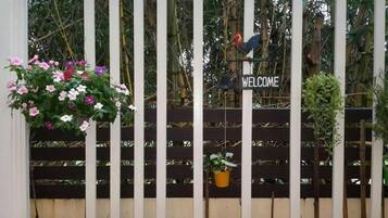 A wooden fence with a 'WELCOME' sign, a hanging flower arrangement, and a bird perched on the fence.