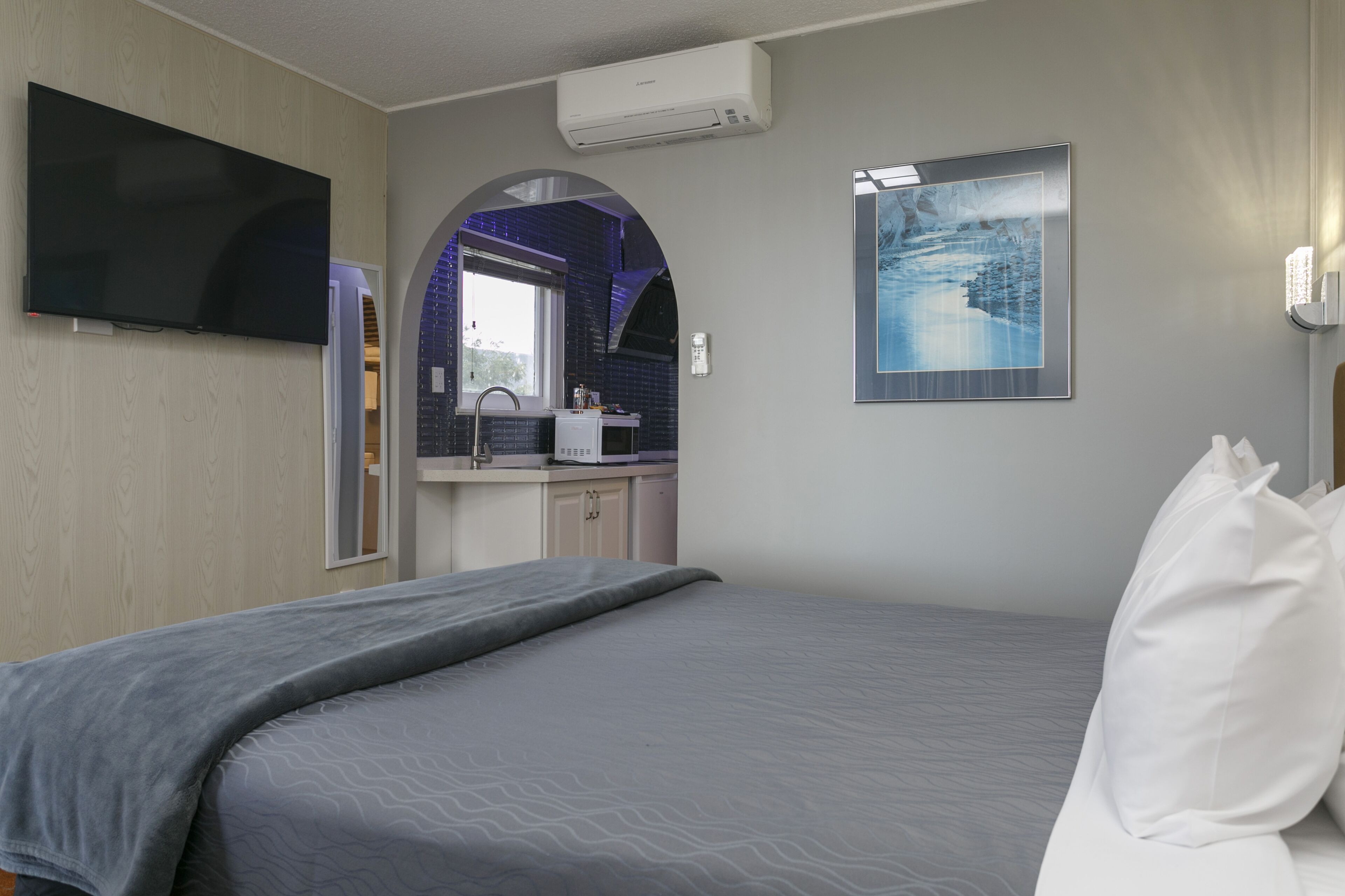 A hotel room with a bed, a flat-screen TV, a bathroom with a sink and mirror, and a framed picture on the wall.