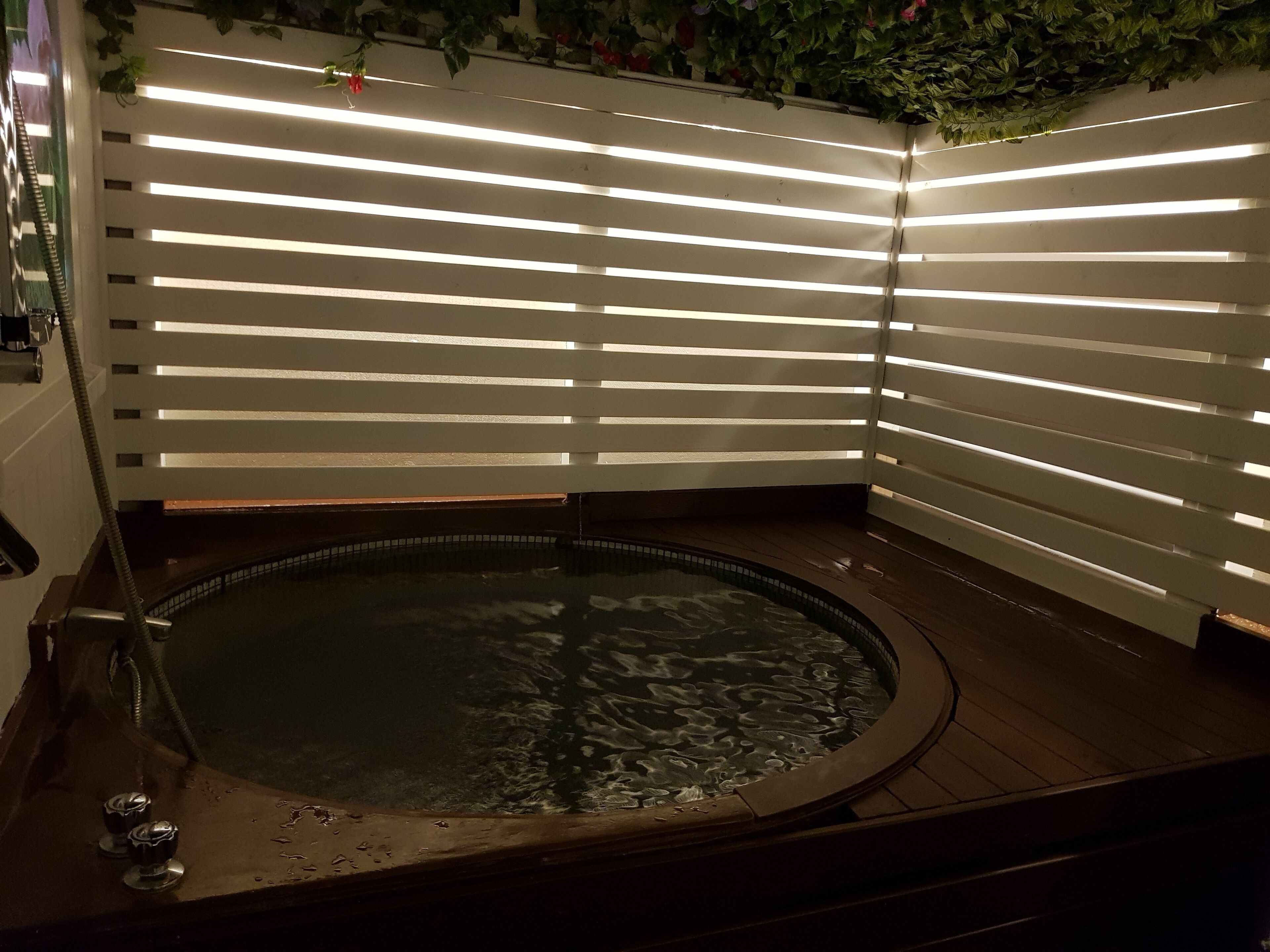 Un jacuzzi con cubierta de madera y un muro blanco de listones detrás.
