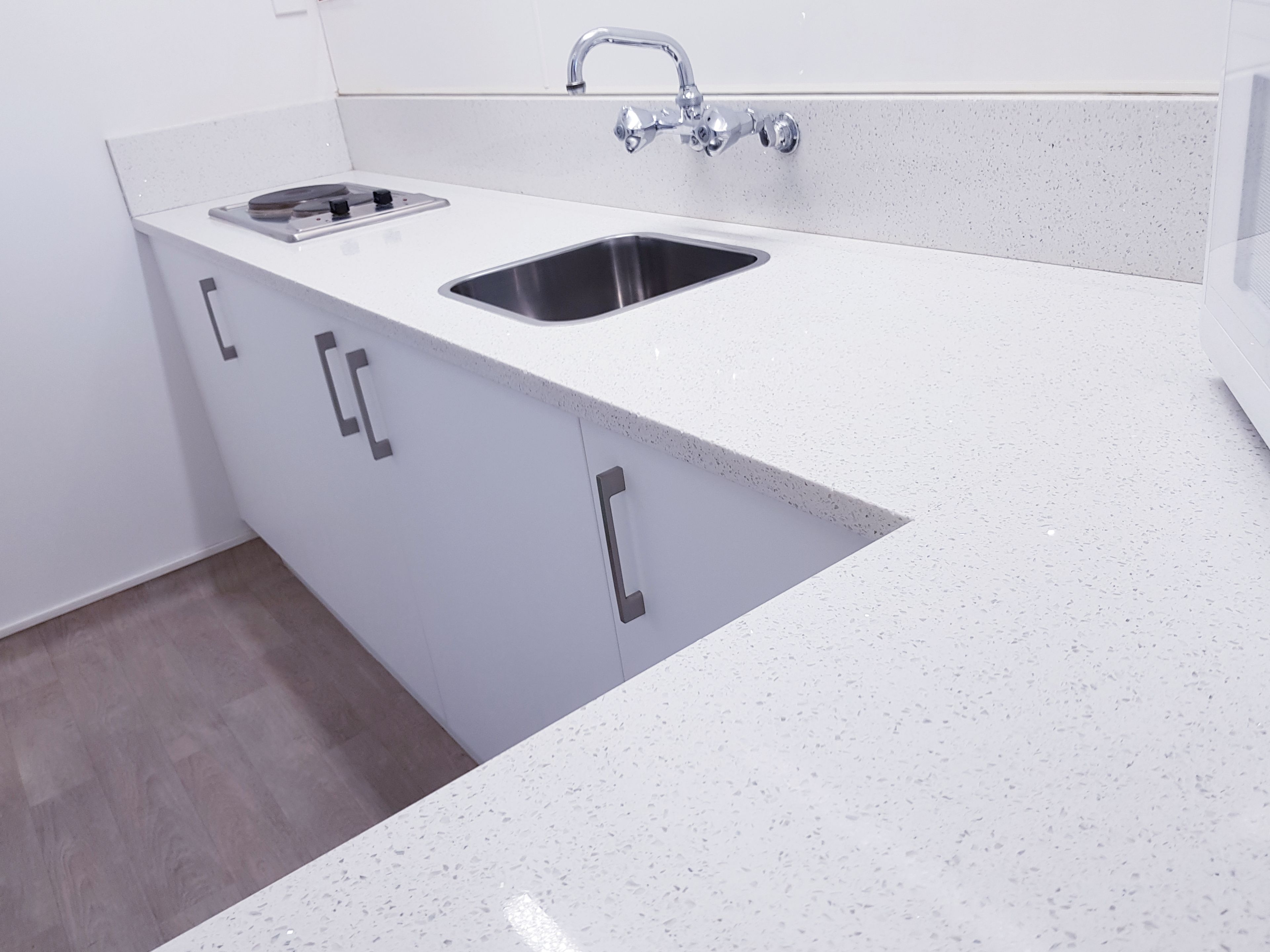 Uma cozinha moderna com bancada branca, duas pias de aço inoxidável e uma torneira.