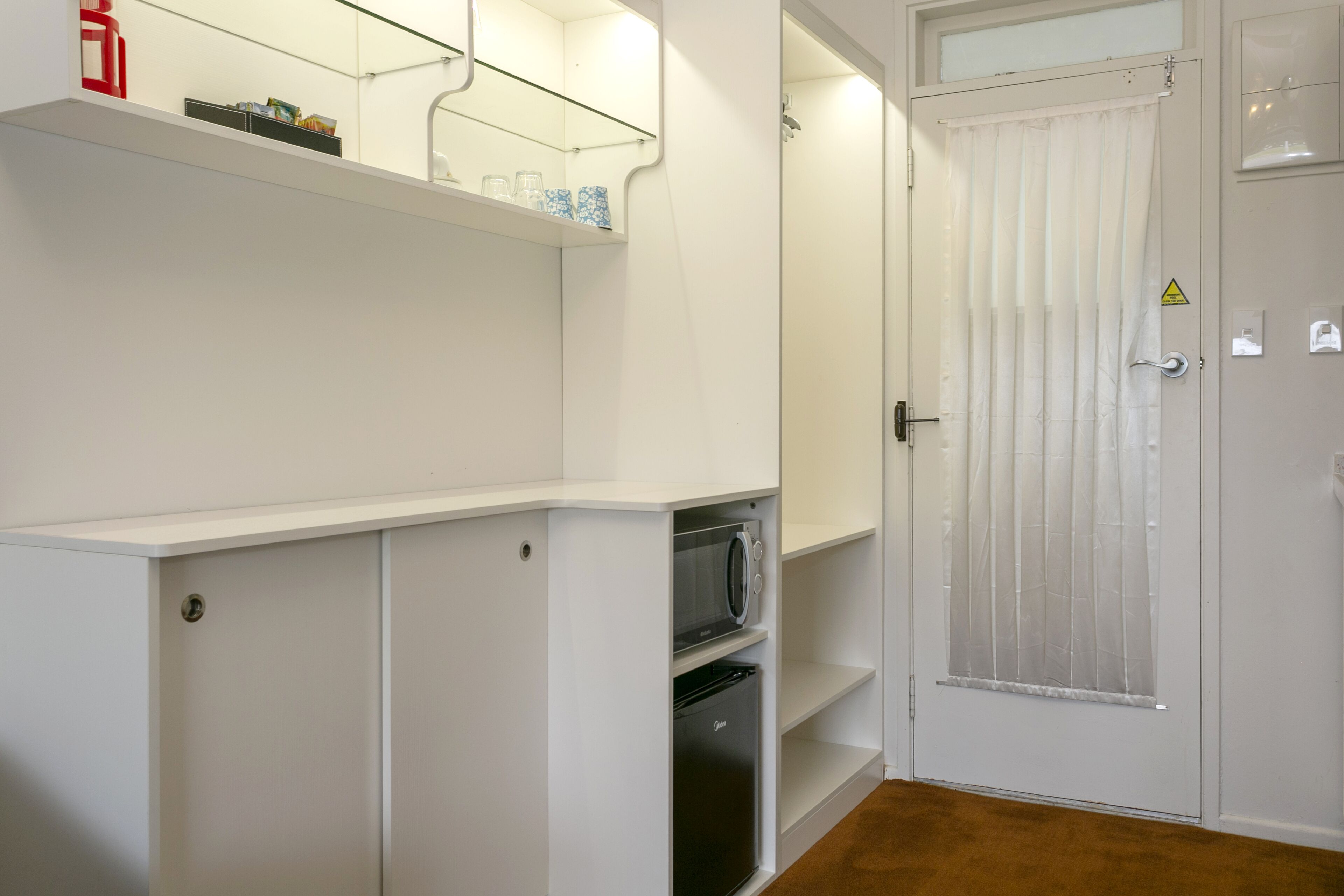 A compact room with a microwave, a refrigerator, and a door with a window.