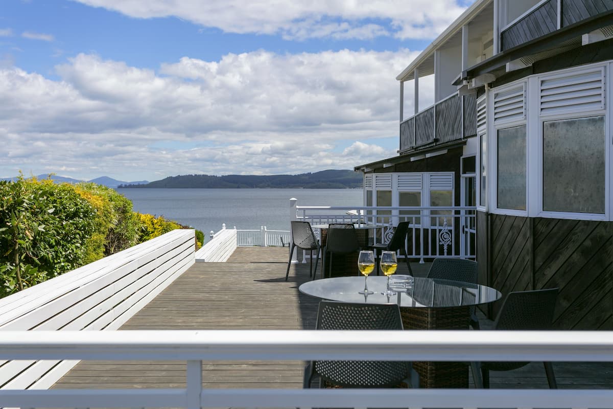 Une terrasse en bois avec des sièges extérieurs, offrant une vue sur une étendue d’eau et sur des collines lointaines.