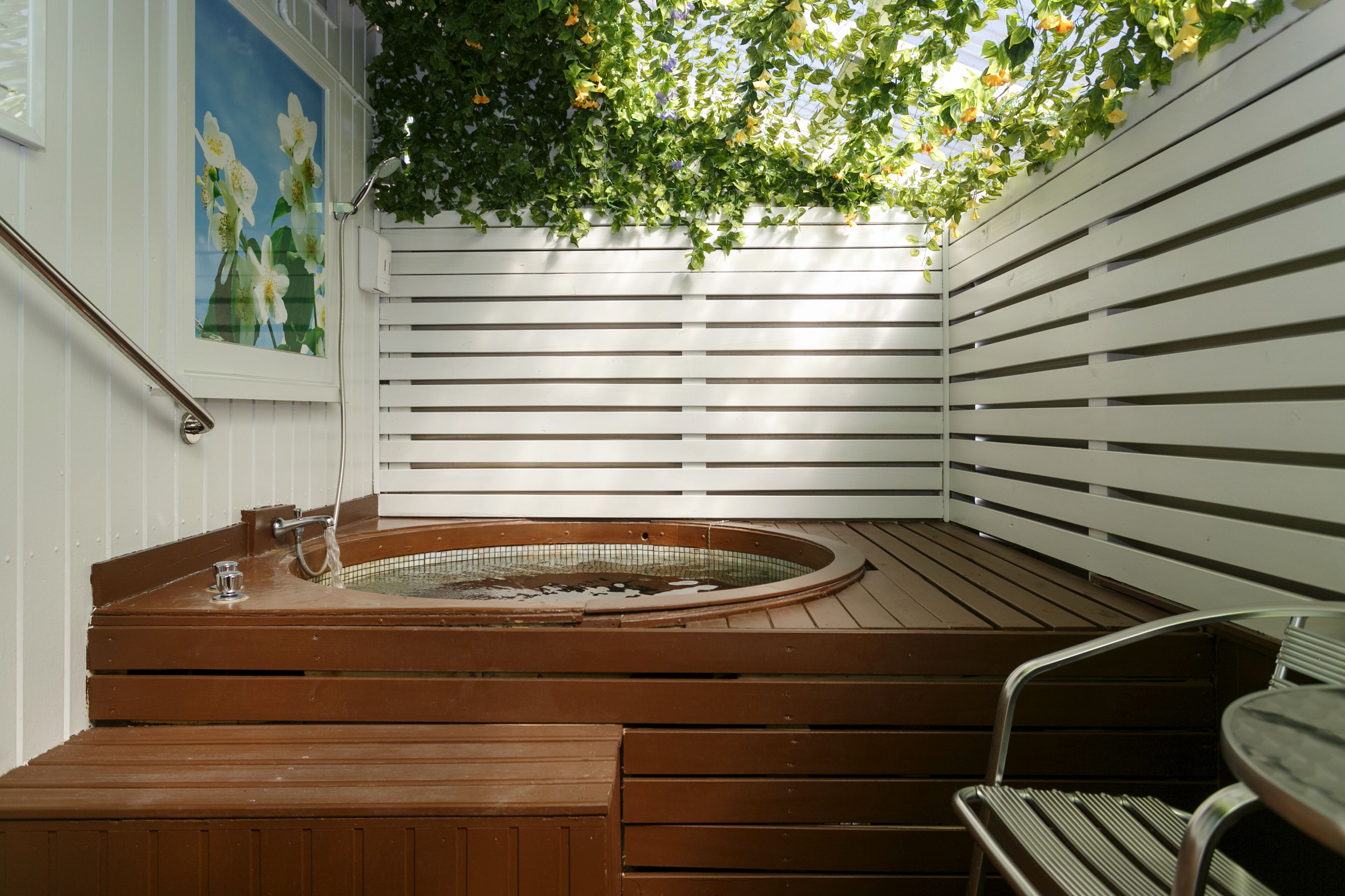 Un bain à remous en bois, avec un escalier en métal, une porte en verre et une peinture de fleurs sur le mur.
