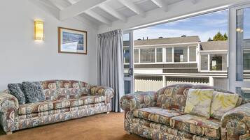 A modern living room with two patterned sofas, a large window with a view of a house, and a framed picture on the wall.