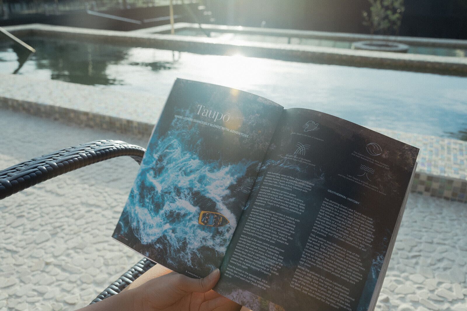 Pessoa segurando um folheto com padrão de ondas, ao ar livre perto de uma piscina.