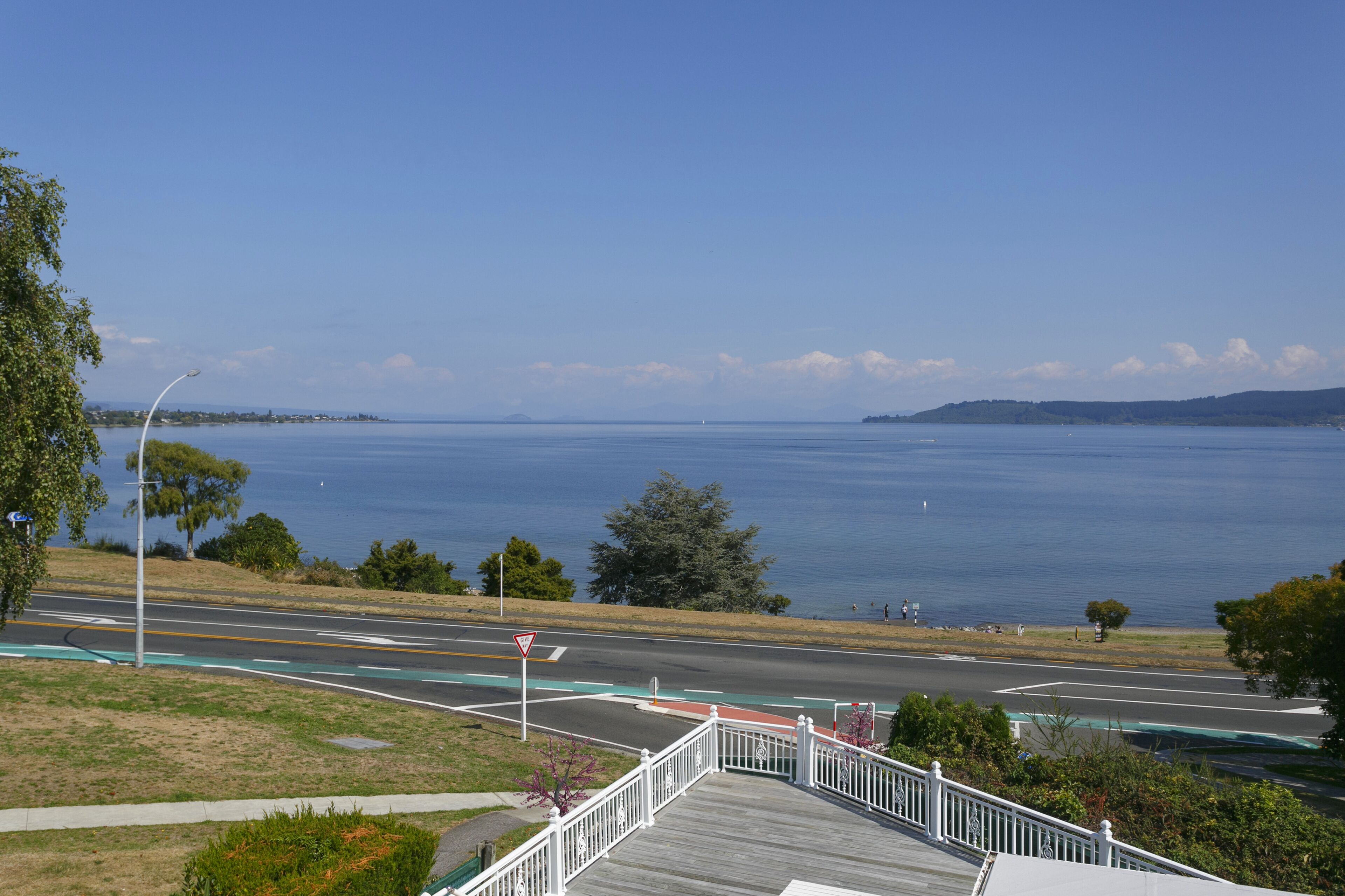 A coastal road with a pedestrian bridge, a clear view of the sea, and a distant shoreline.
