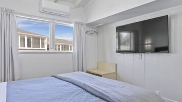 A bedroom with a bed, a TV mounted on the wall, a window with curtains, and a small wooden table.