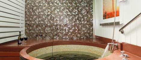 A hot tub with a tiled wall behind it, a bottle of wine, and two wine glasses on the side.