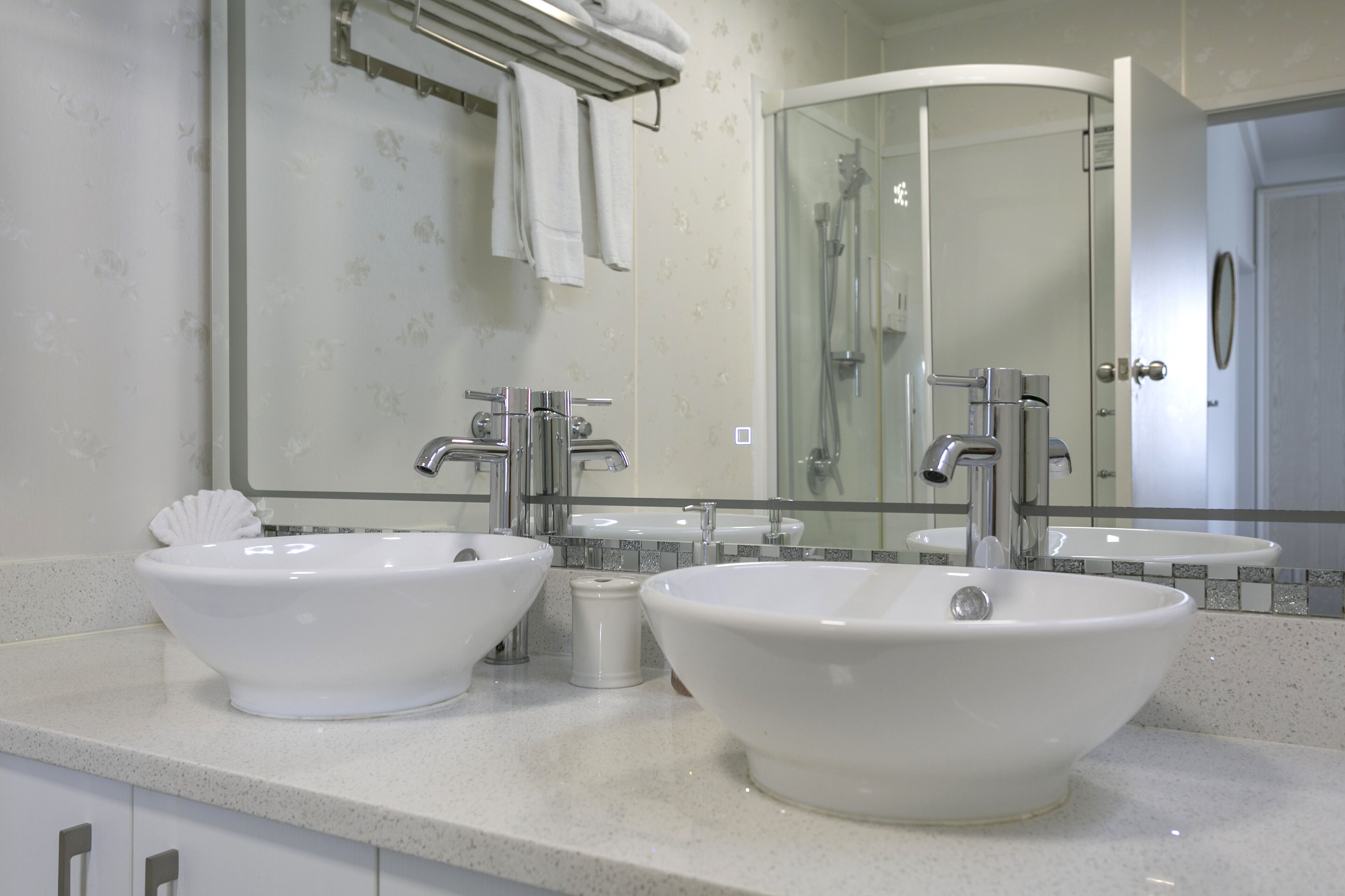 A bathroom with two large white sinks, a glass shower enclosure, and a mirror above the sinks.