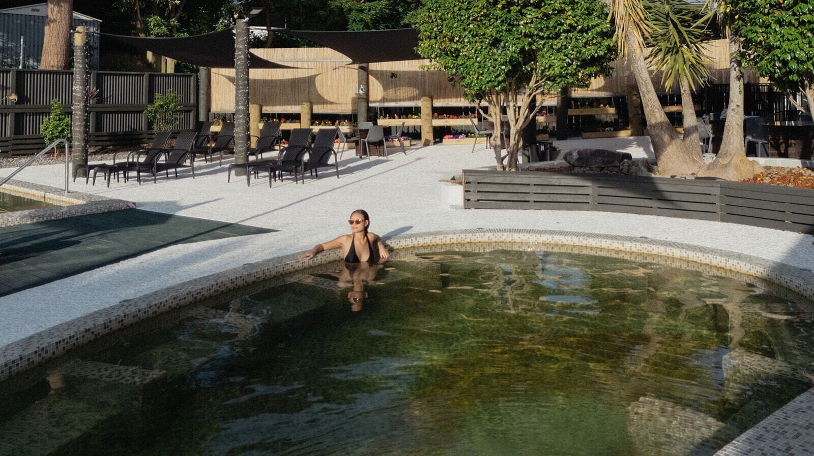 A pool area with lounge chairs and a person relaxing in the water.