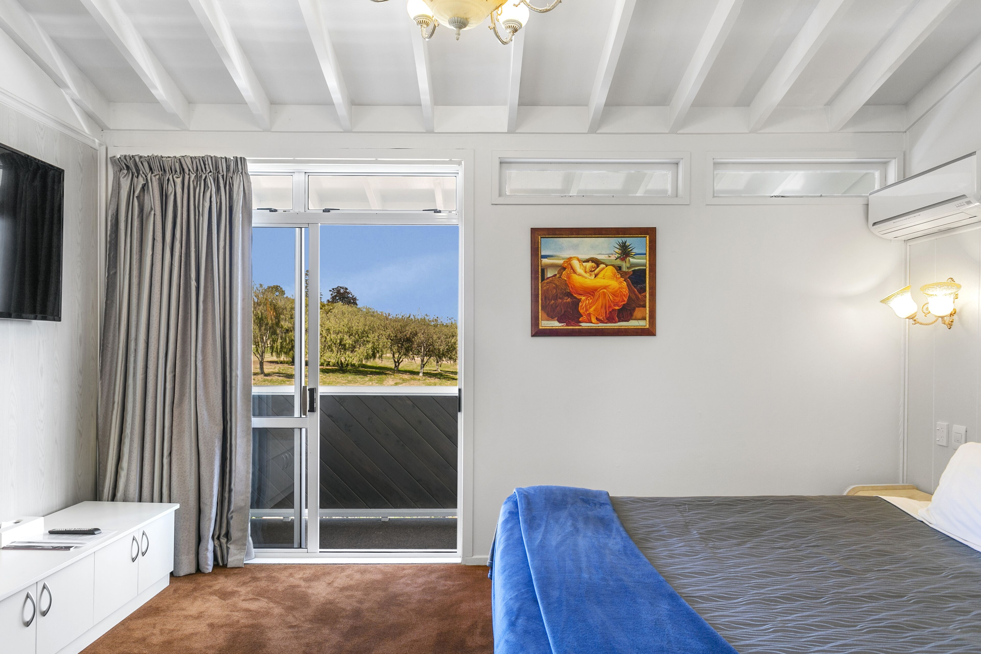 Une chambre à coucher avec un lit, une fenêtre avec des rideaux, un tableau au mur et un ventilateur de plafond.