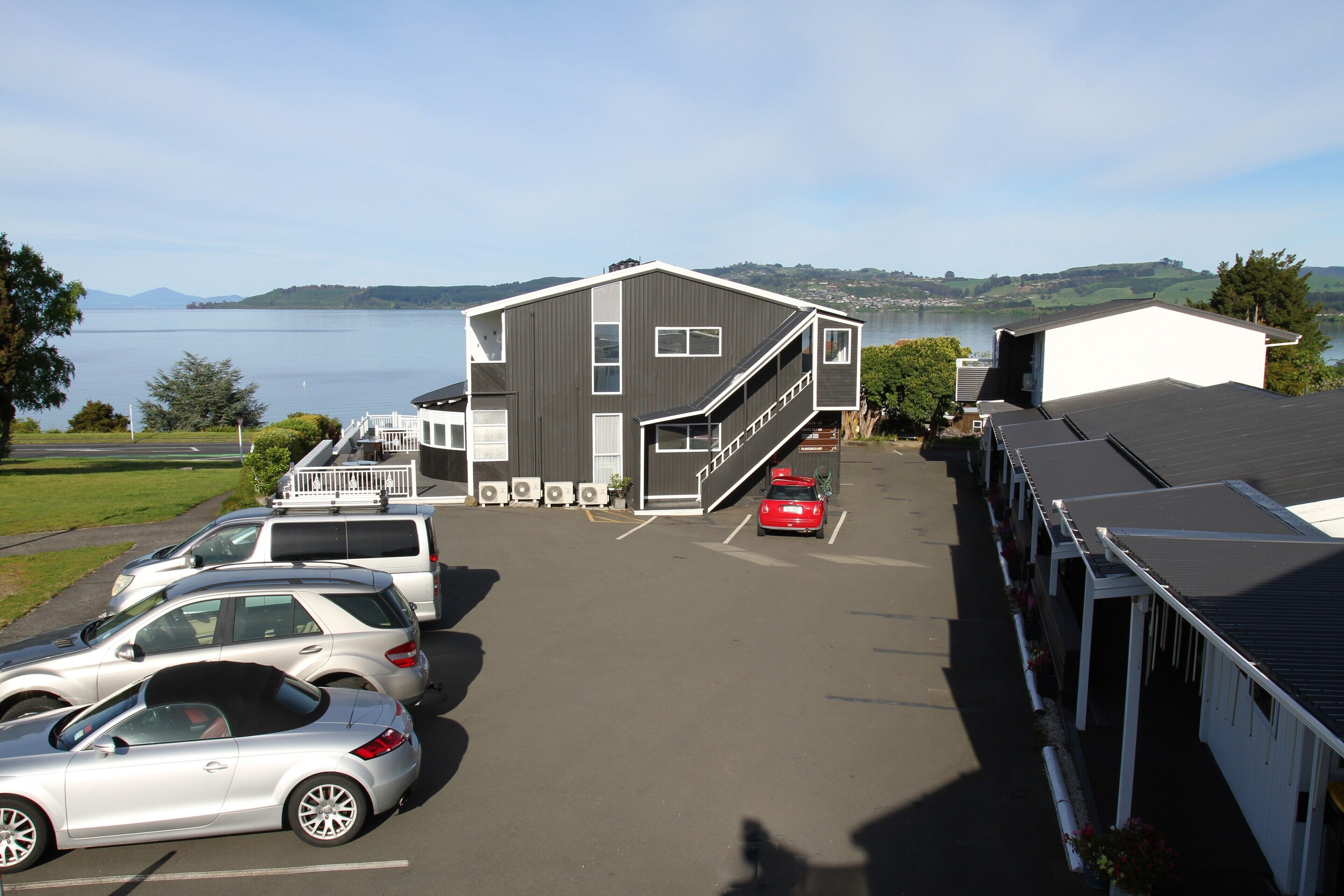 A parking lot with several cars, a building with a staircase, and a view of a lake and hills in the background.