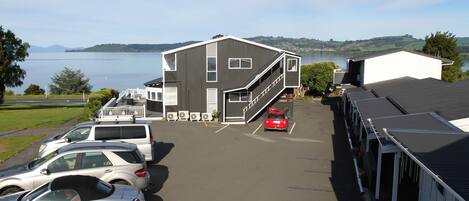 A parking lot with several cars, a building with a staircase, and a view of a lake and hills in the background.
