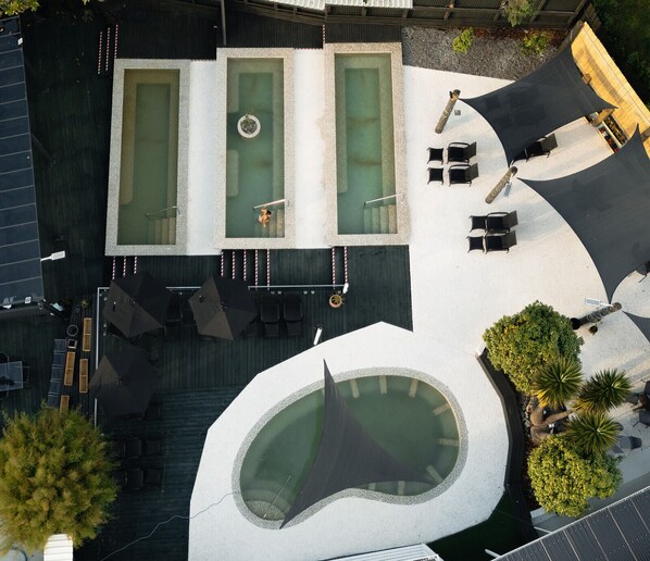 Vue aérienne d’un espace piscine sur le toit, comprenant trois piscines rectangulaires, une piscine circulaire et des espaces de détente en plein air.
