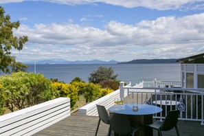 Une terrasse avec une table et des chaises, donnant sur un plan d’eau et des montagnes.