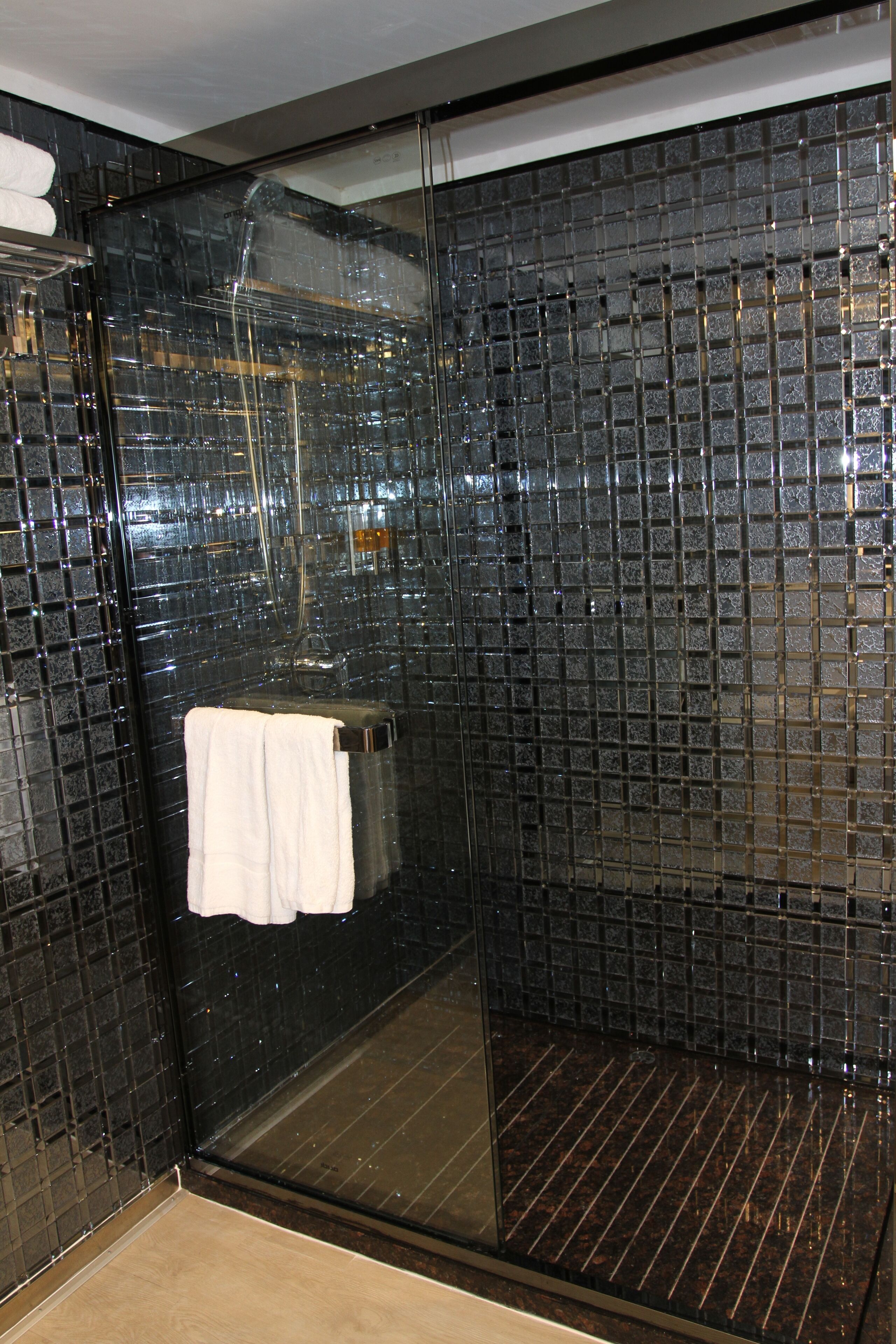 A glass-enclosed shower with a glass door and a towel hanging on the door handle.
