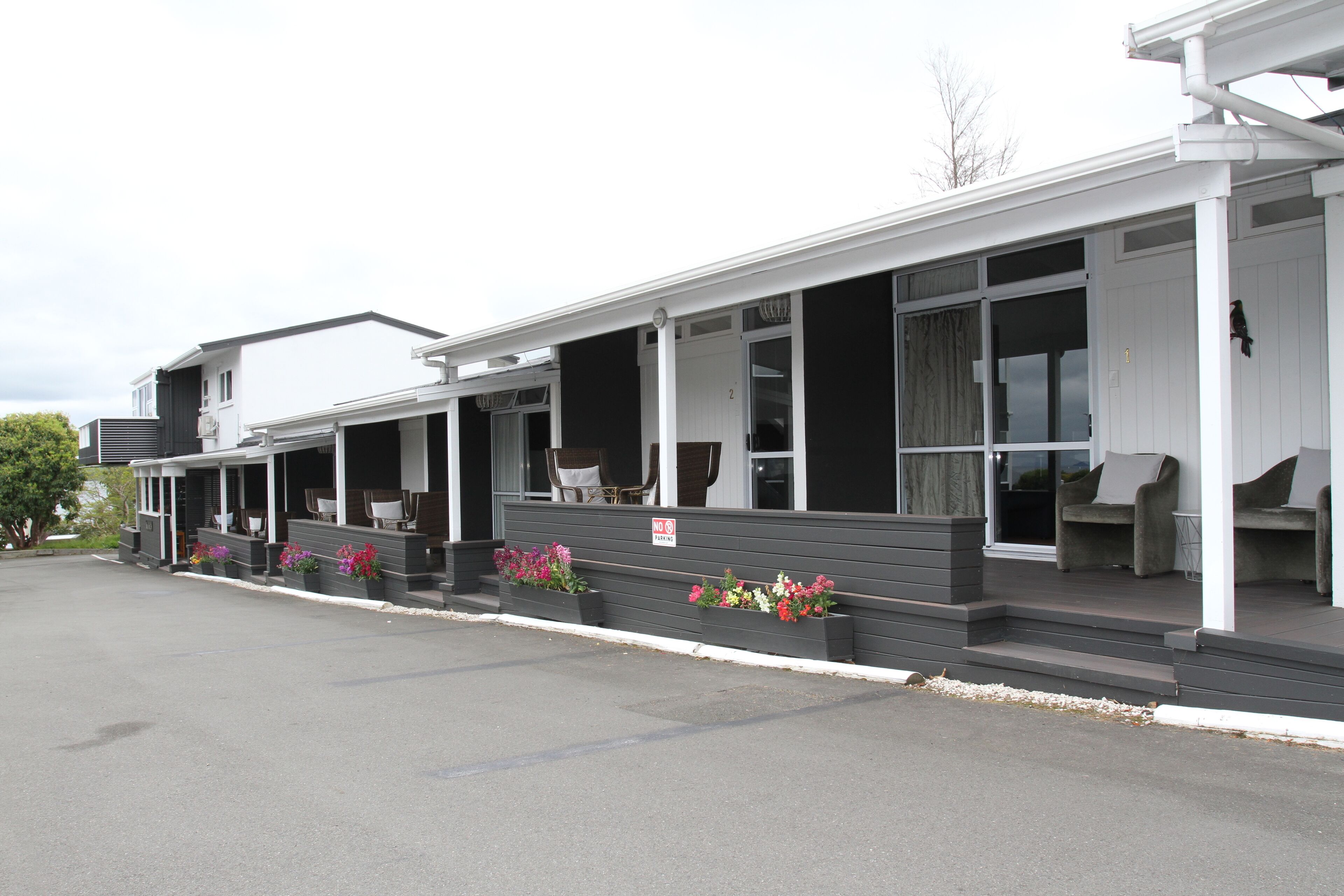 Un motel con un porche cubierto, varias habitaciones y macetas con flores.