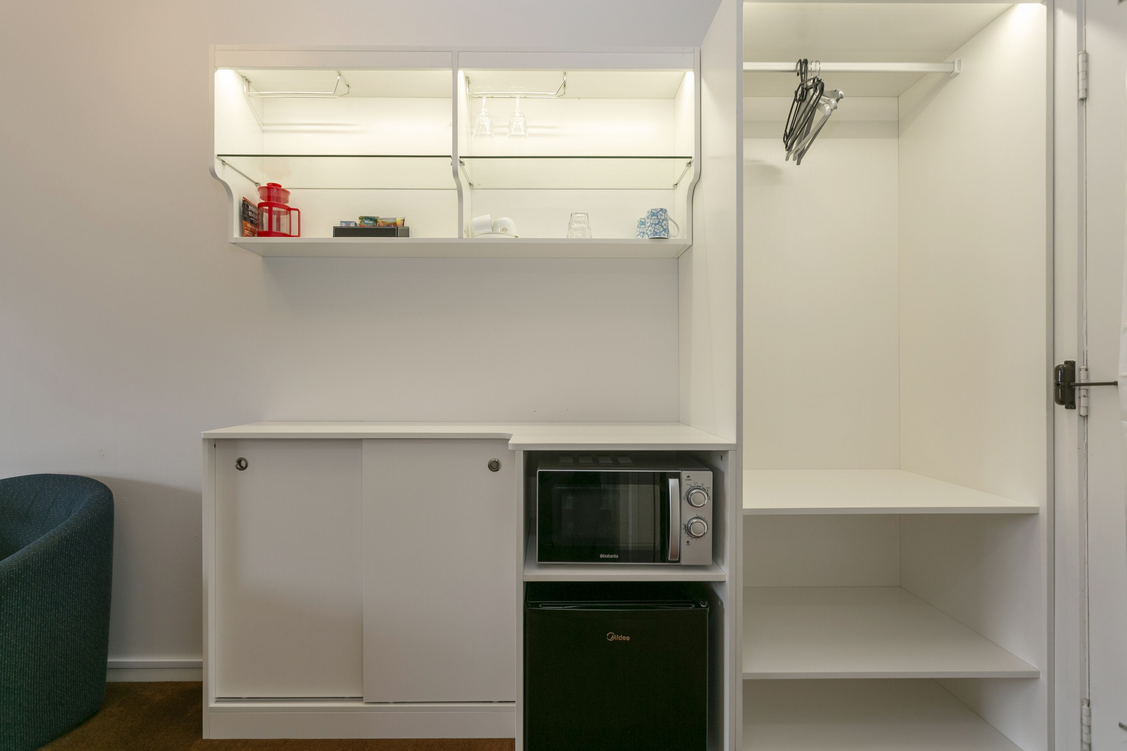 Una kitchenette compacta con microondas, mini refrigerador y estantes superiores.