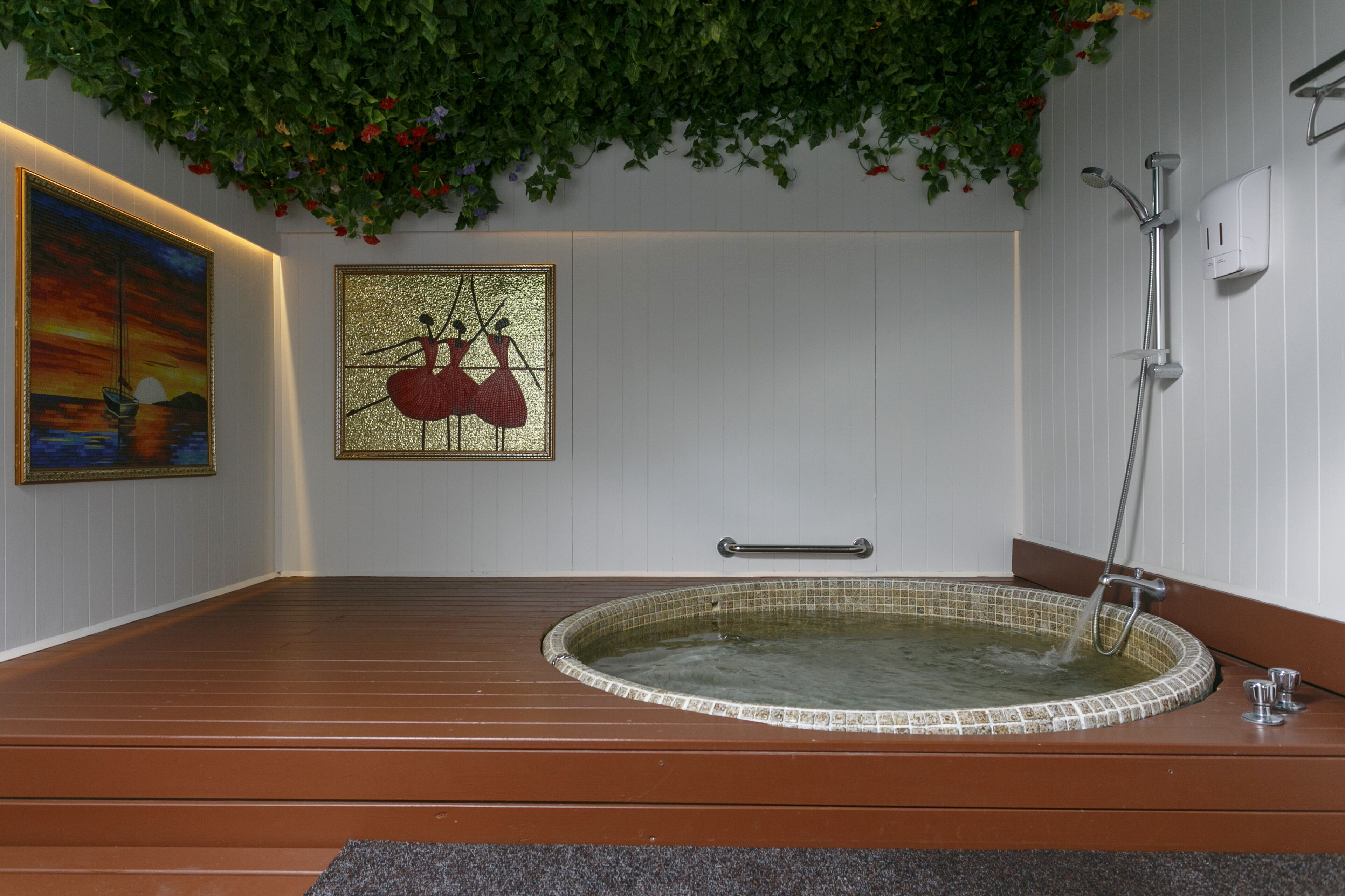 A spa room with a hot tub, wooden flooring, and wall-mounted artwork.