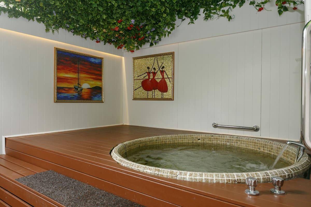 Une salle de spa avec un banc en bois, un jacuzzi et deux œuvres d’art encadrées accrochées au mur.