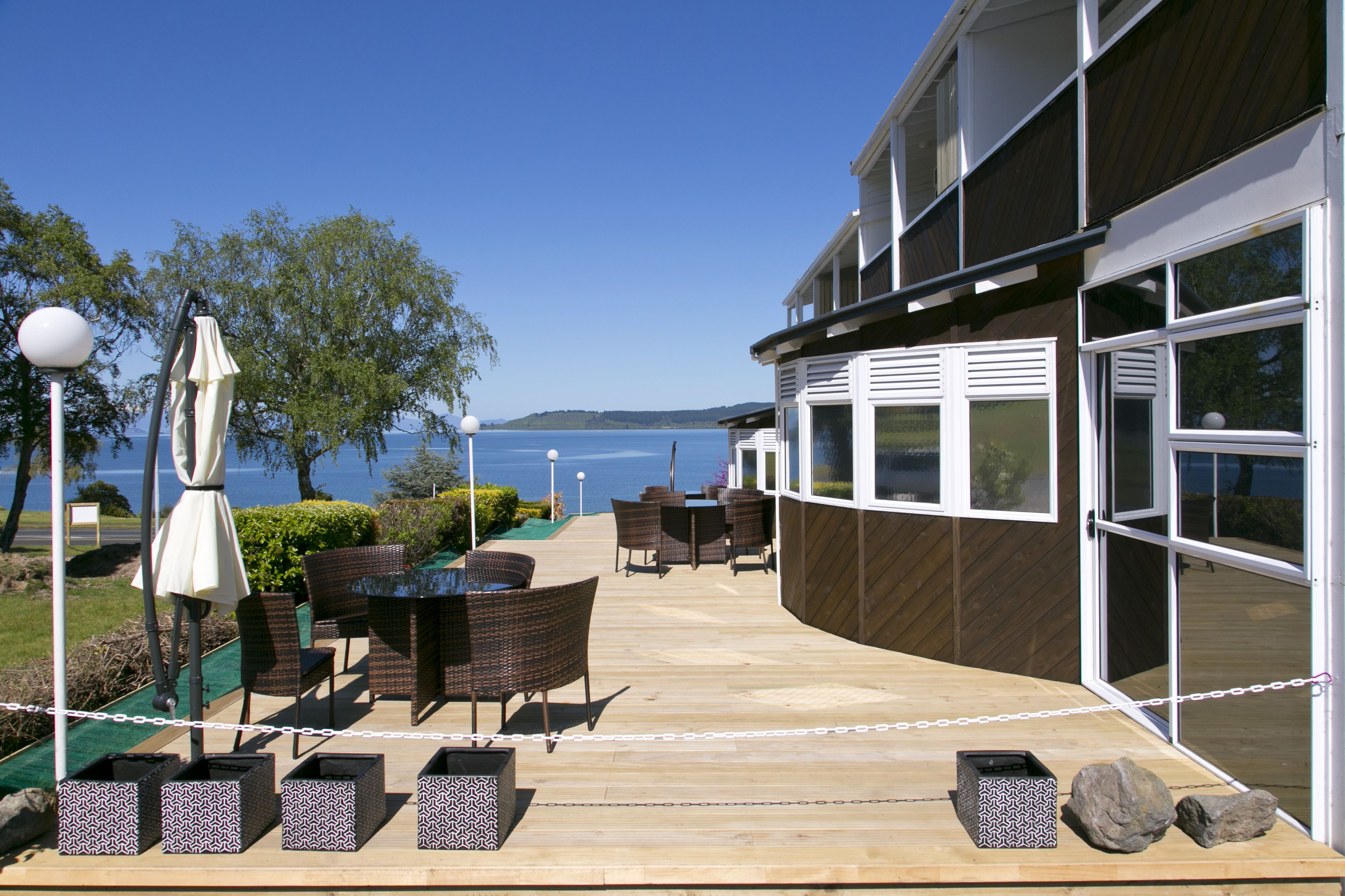 An outdoor patio with wicker furniture, a table, and chairs, overlooking a body of water.