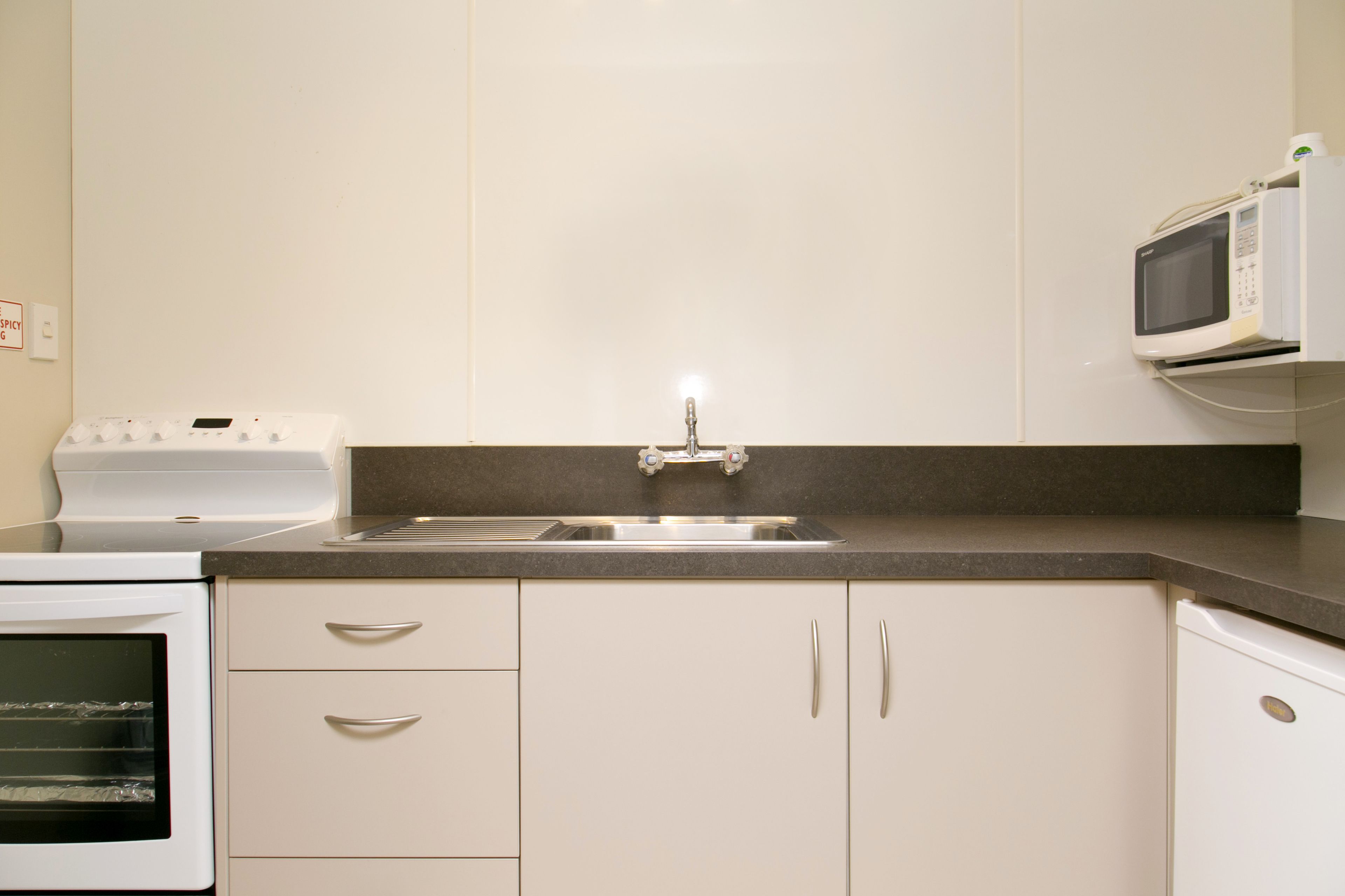 A kitchen with a built-in oven, a microwave, a sink, and white cabinets.