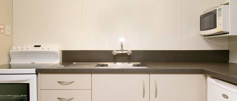 A kitchen with a built-in oven, a microwave, a sink, and white cabinets.
