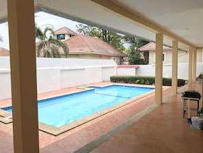 A swimming pool with a tiled deck, surrounded by a white wall and a hedge. - Pattaya Longstay Village 3 (Bang Lamung)