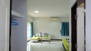 A hotel room with a bed, a small sofa, a window with curtains, and an air conditioning unit. - Pattaya Longstay Village 3 (Bang Lamung)