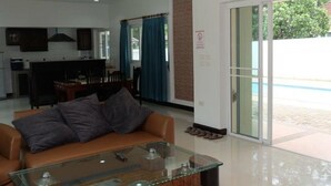 A modern living room with a glass coffee table, a brown sofa, and a ceiling fan. - Pattaya Longstay Village 3 (Bang Lamung)