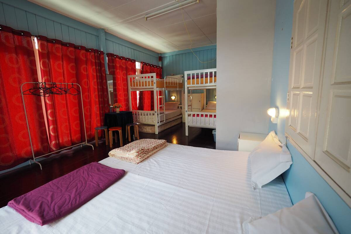 Ein Hotelzimmer mit Etagenbetten, einem Bett mit violetter Decke und einem roten Vorhang.